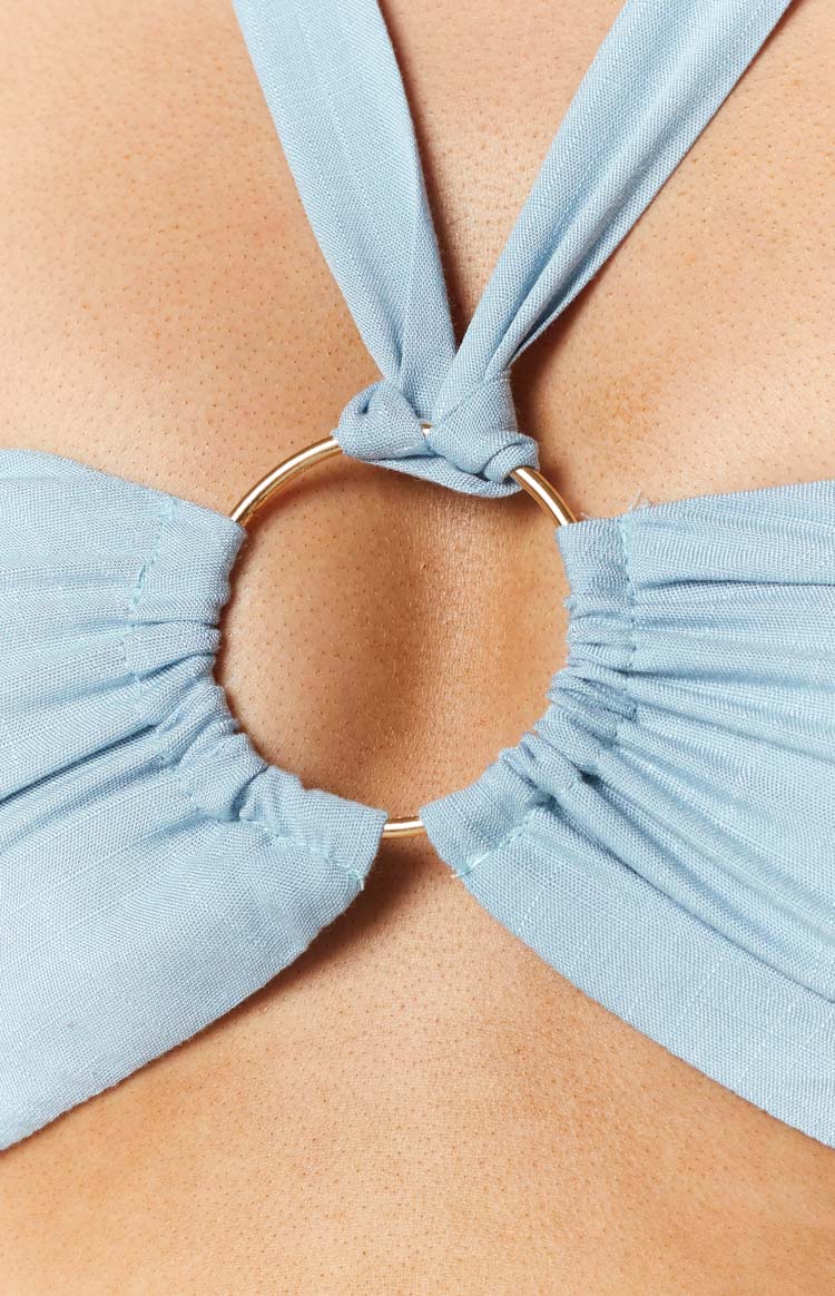 Close-up of the gold O-ring detail on a light blue halter top, with gathered fabric and tied halter straps