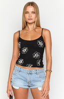 Model wearing a black basic tank top with white beaded flower details paired with a denim mini skirt