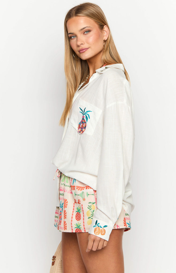 Side view of a white oversized long sleeve shirt with embroidered pineapple on the chest pocket and oranges on the cuff