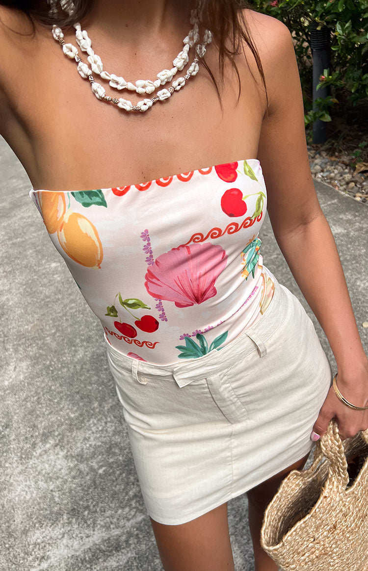 Close-up of the strapless neckline with red scalloped trim and colourful fruit and shell print on a light bodysuit