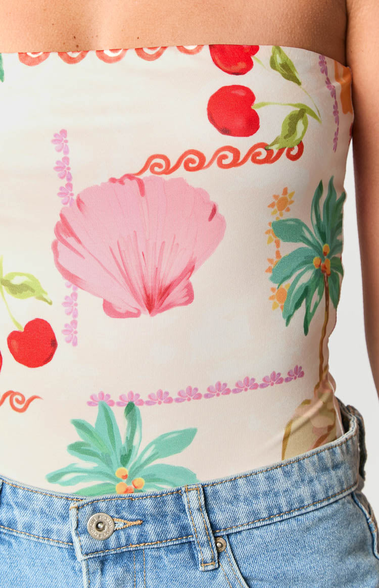 Close-up of the cream bodysuit's tropical print with red cherries, a large pink shell, and palm trees