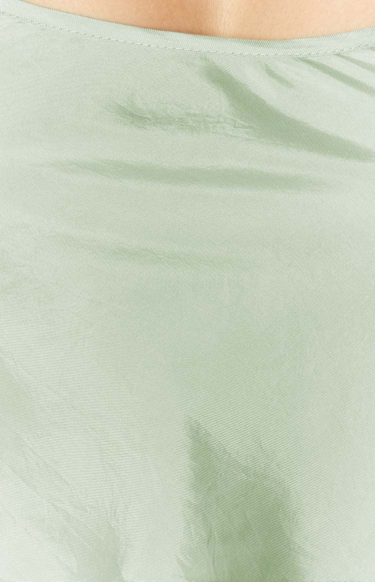 Close-up of the sage green silky fabric with subtle texture and fine stitching along the neckline