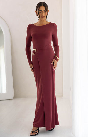 Full length view of a burgundy long sleeve maxi dress with a boat neck and a gold abstract buckle at the wrap waist