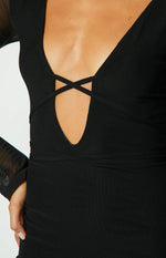 Close-up of the black maxi dress showing the deep V-neckline with criss-cross straps, wrapped waist, and sheer long sleeve