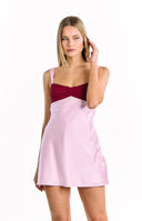 A feminine color-blocked mini-dress with a dark red bust featuring a twisted detail and a light pink satin-like skirt. Our dress has wide pink shoulder straps.