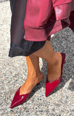 Angled view of cherry red patent mule heels with a pointed toe, V-cut vamp, and low kitten heel