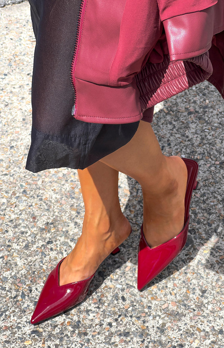 Angled view of cherry red patent mule heels with a pointed toe, V-cut vamp, and low kitten heel