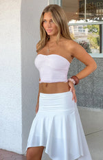 Side view of a pink and white polka dot strapless top with a ruched bust, small bow, and ruffled cropped hem