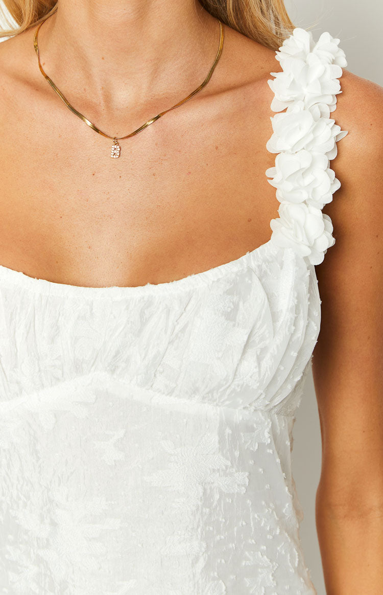 Close-up of the white mini dress showing the textured fabric, gathered bust, and 3D floral shoulder strap