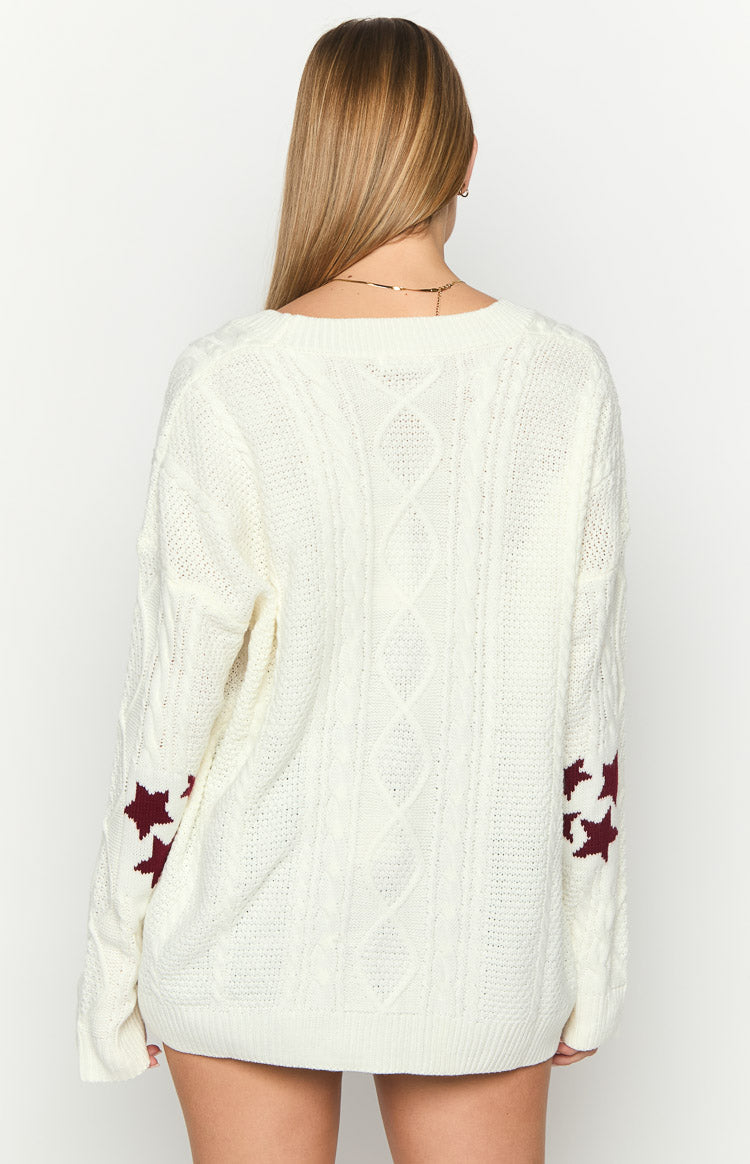 Back view of an oversized white cable knit cardigan with a round neck and maroon star patterns on the sleeves