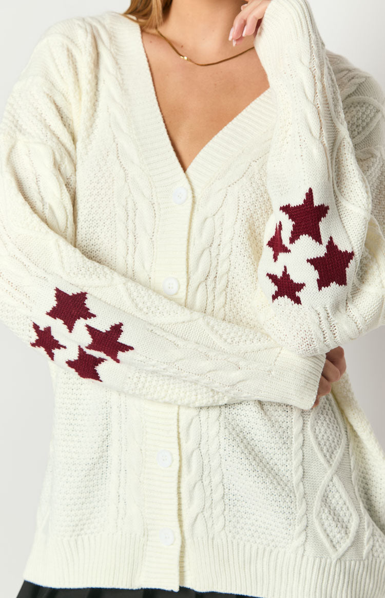 Close-up of the cream cable knit cardigan with burgundy star pattern on the long sleeves and white buttons