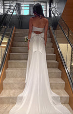 Rear view of a white strapless maxi dress with a large back bow and cutout detail, flowing into a long train