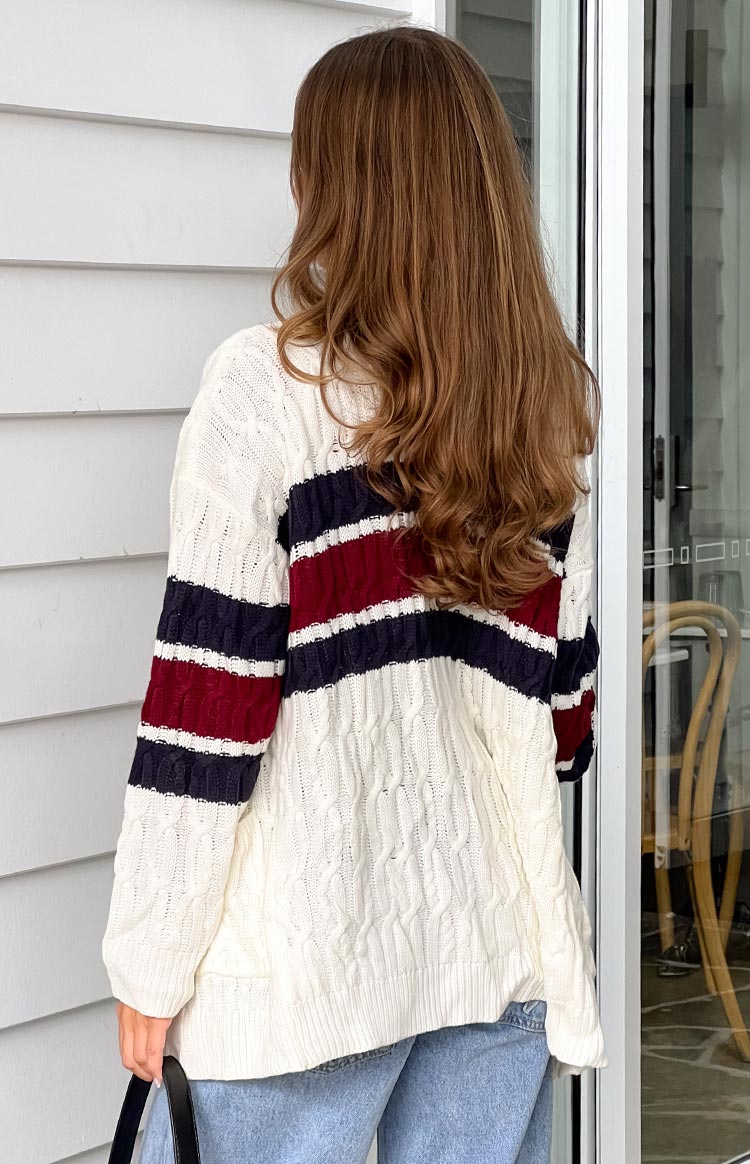 Rear view of a cream cable knit cardigan with red and navy stripes across the back and sleeves