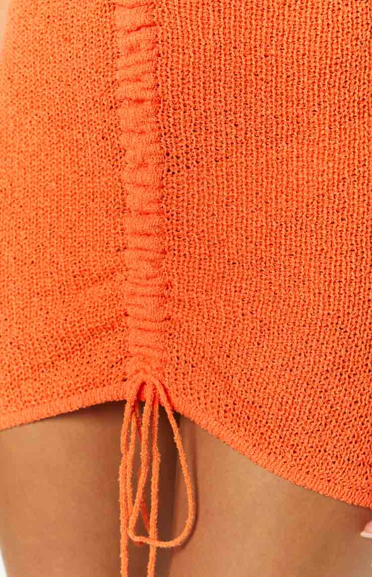 Close-up of the orange knit fabric showing the ruched side detail and adjustable tie strings of the mini dress