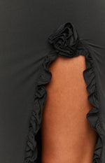 Close-up of the black maxi dress showing a fabric rose and ruffled trim along a leg cutout