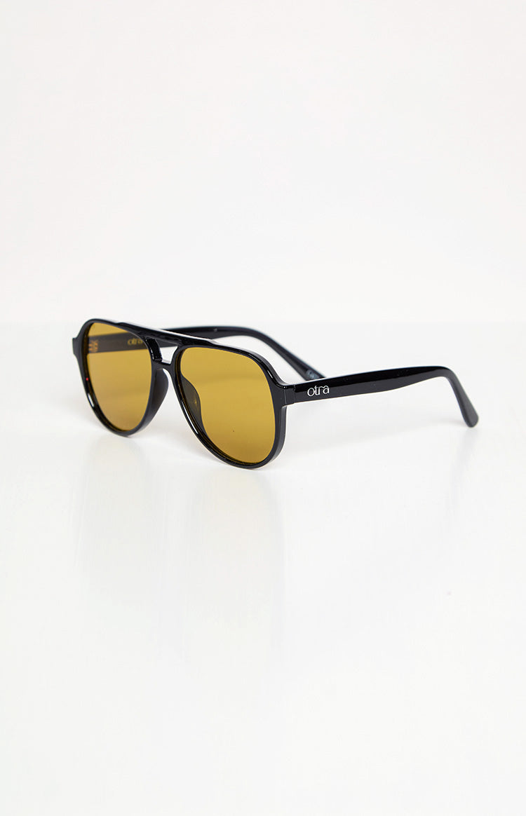 Angled side view of black aviator sunglasses with amber lenses and a visible brand logo on the temple arm