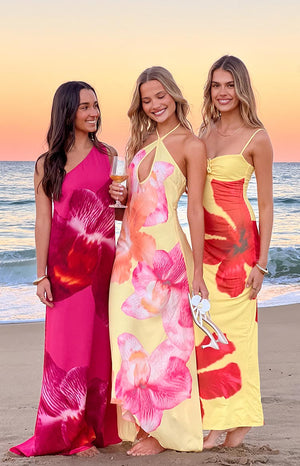 Flowy hot pink one-shoulder maxi dress with a large dark orchid print, flowing to the sand