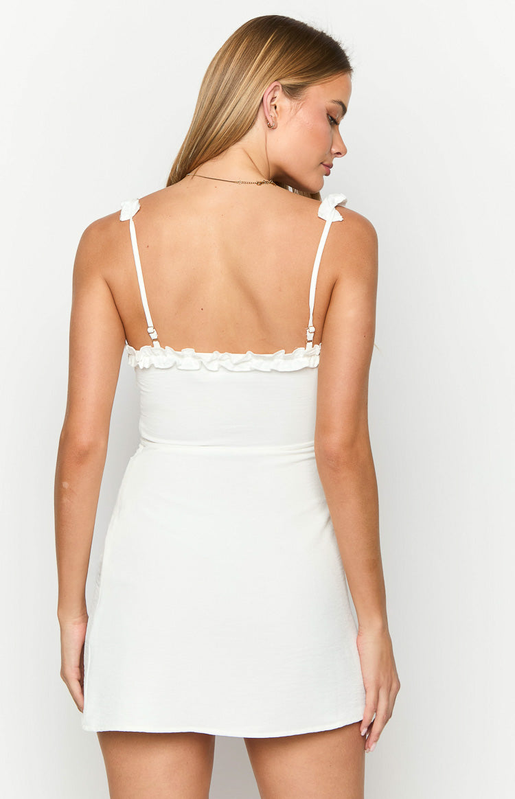 Rear view of a white mini dress with ruffled trim along the back bodice and thin adjustable spaghetti straps
