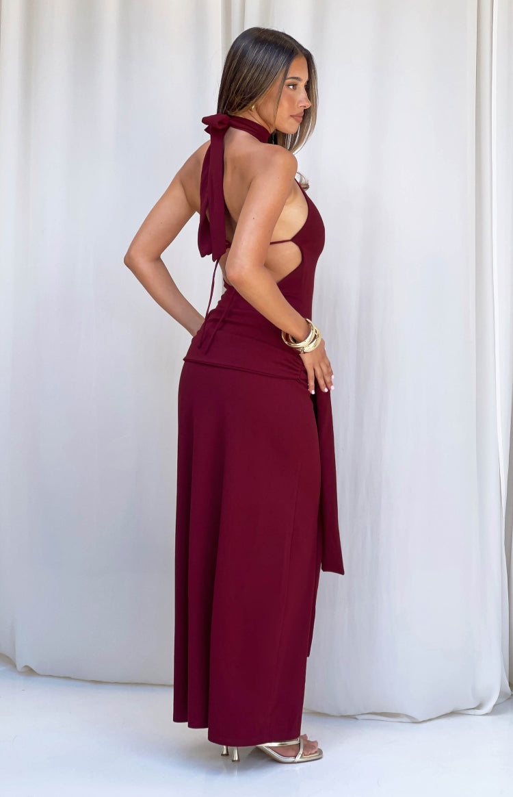 Side view of a burgundy jersey formal dress showing the halter neck tie, open back, side cutouts, and ruched maxi skirt