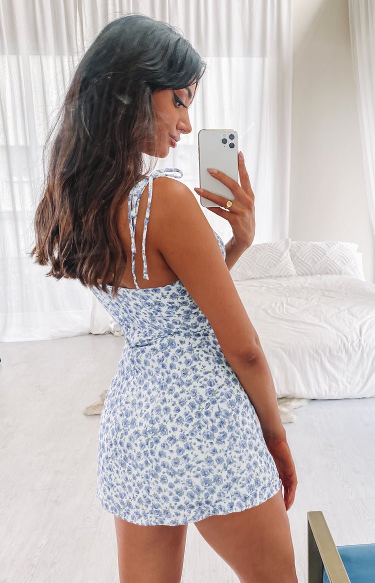 White mini dress with blue floral print, delicate tie-shoulder straps, and a fitted A-line silhouette