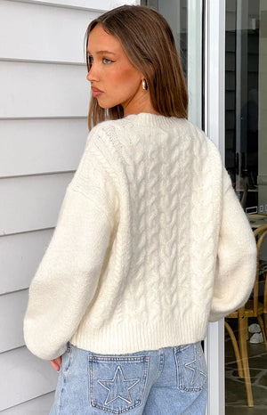 Rear view of a cream cable knit cardigan showing the textured back, dropped shoulders, and ribbed hem