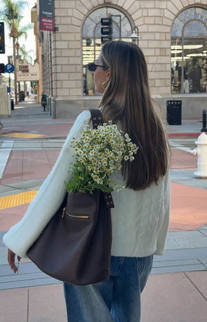 A female model wearing an off-white button-up knit cardigan with a round neckline cable-knit texture and cuffed sleeves.