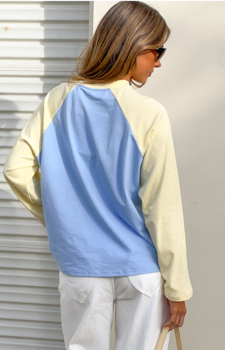 Rear view of a blue and yellow contrast raglan sleeve top with long sleeves and a relaxed fit
