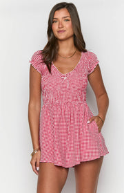 Front view of a red gingham playsuit with a shirred bodice, V-neck, ruffled cap sleeves, and side pockets