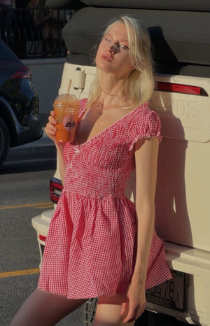 Red gingham playsuit with a V-neck, shirred bodice, short ruffled puff sleeves, and flowy shorts