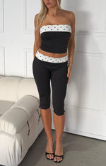 Side view of black fitted capris with a white polka dot waist band and split hem detail