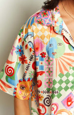 Close-up of the colourful abstract print satin shirt featuring sun and moon faces, flowers, and geometric patterns