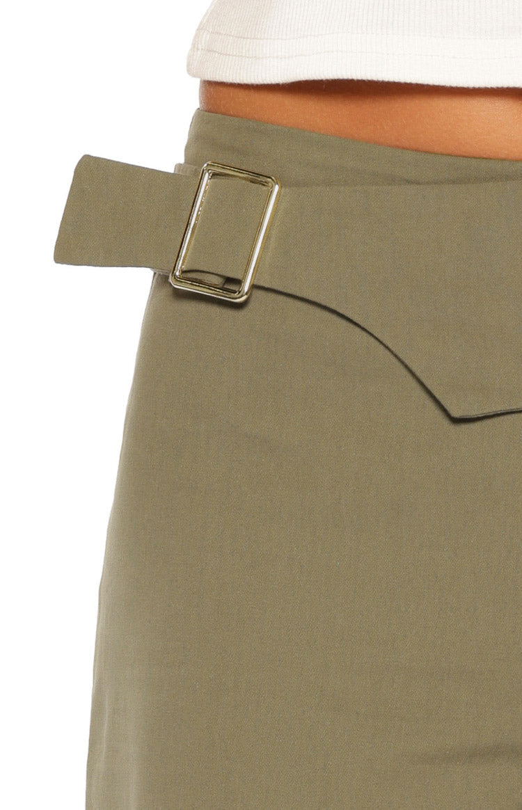 Close-up of the green pants' waist with a gold rectangular buckle and a curved fabric overlay detail