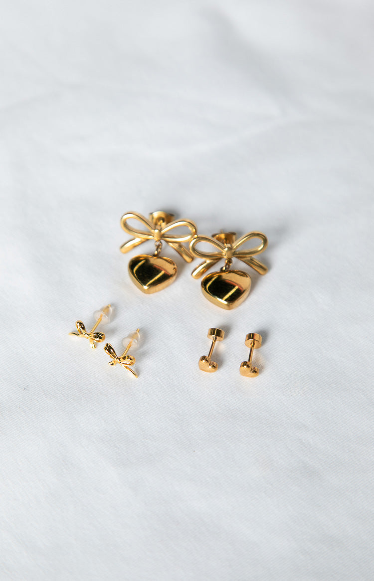 Three pairs of gold earrings: bow and heart drop earrings, small bow studs, and small heart studs