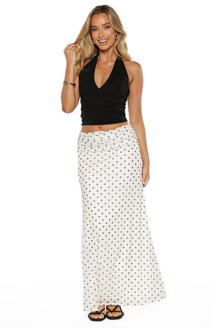 A full-length studio shot from the waist down of our model wearing a floor-length white maxi skirt with a small black polka-dot pattern. This skirt features a wide horizontally ruched waistband and falls in a straight fluid silhouette.