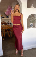 Burgundy satin maxi skirt with a fitted waist and a subtle diagonal drape detail on the hip
