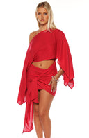 Close up of a girl wearing a red mini dress with an asymmetric sleeve and wrap detail at te skirt. The perfect choice for a christmas celebration or party!