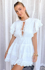White mini dress with high neck, tie-front V-cutout, pintuck bodice, and tiered flutter sleeves with broderie anglaise