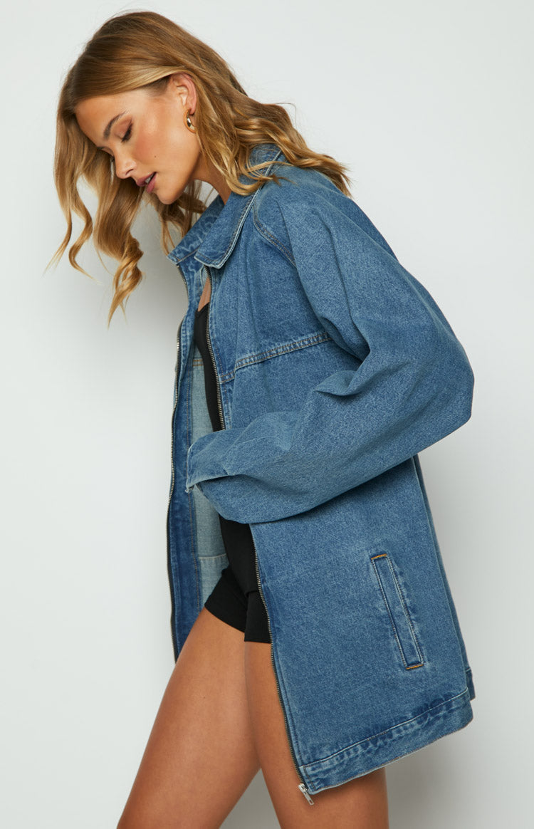 Front view of a blue oversized denim jacket, unzipped to show the silver zipper and relaxed fit