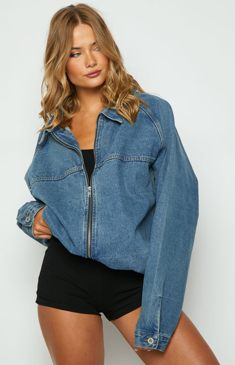 Rear view of an oversized blue denim jacket with raglan sleeves, visible stitching, and rolled-up long sleeves