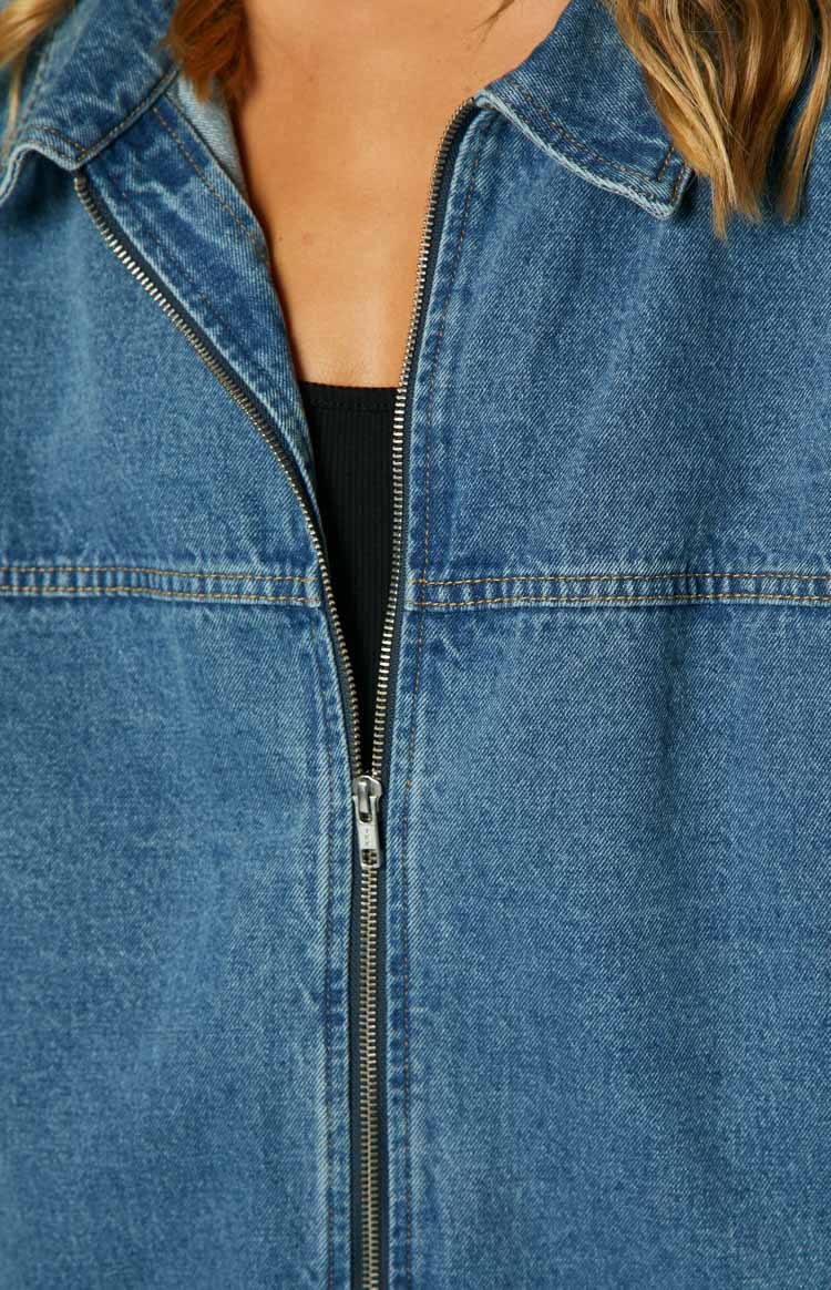 Blue oversized denim jacket with a classic collar, front zipper, dropped shoulders, and buttoned cuffs