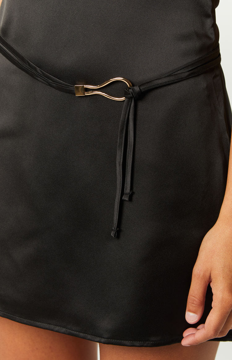 Close-up of the black tie-belt with a gold abstract buckle on a black mini dress
