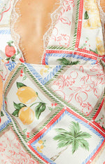 Close-up of the white satin mini dress's V-neckline with lace trim and the colourful Roma print of lemons, strawberries, and palm trees