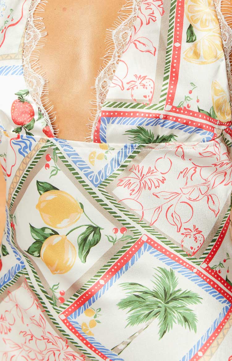 Close-up of the white satin mini dress's V-neckline with lace trim and the colourful Roma print of lemons, strawberries, and palm trees