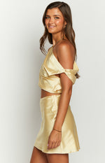 Side view of a yellow satin off-the-shoulder crop top with a draped neckline and halter strap