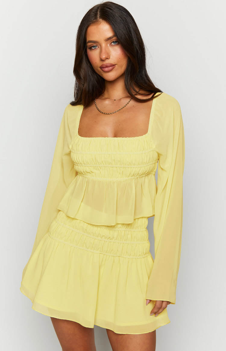 Yellow chiffon long sleeve top with a square neckline, shirred bust, sheer long sleeves, and a peplum hem