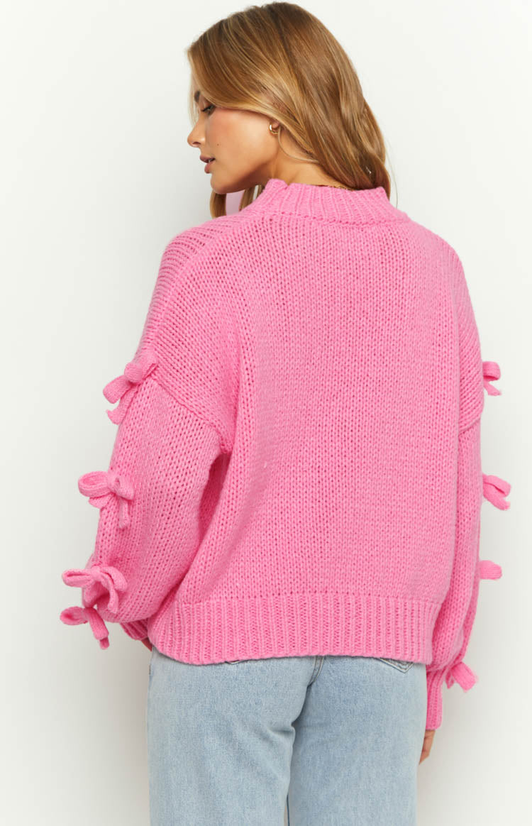 Rear view of a pink chunky knit jumper with a mock neck and bow details on the long sleeves