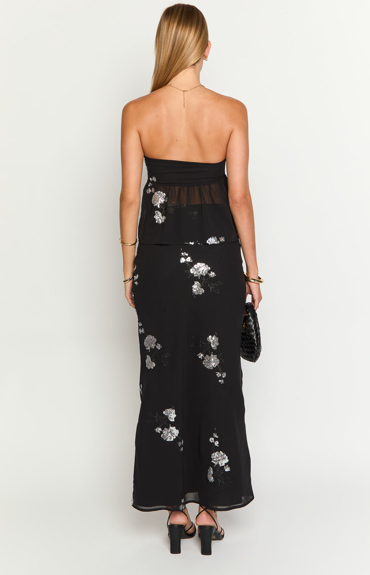 Rear view of a black maxi skirt with silver floral embroidery and a slight flare at the hem