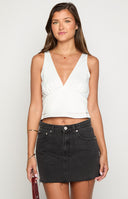 girl wearing a washed black denim mini skirt with raw hem details paired with a white top, gold bracelets and a brown handbag
