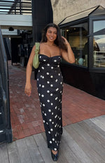 Full length view of a black satin maxi dress with white polka dots, featuring a ruched sweetheart neckline and thin spaghetti straps