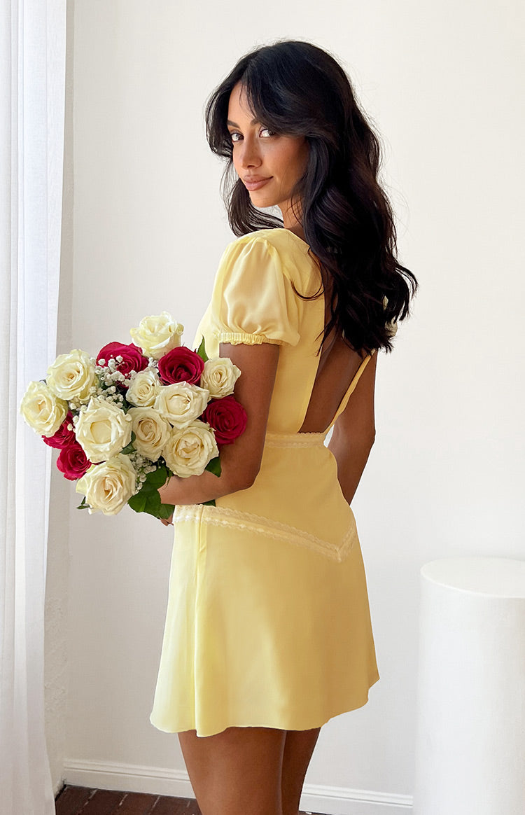 Close-up of the baby yellow mini dress showing the deep V-neck, gathered bodice, delicate lace trim, and sheer puff sleeves